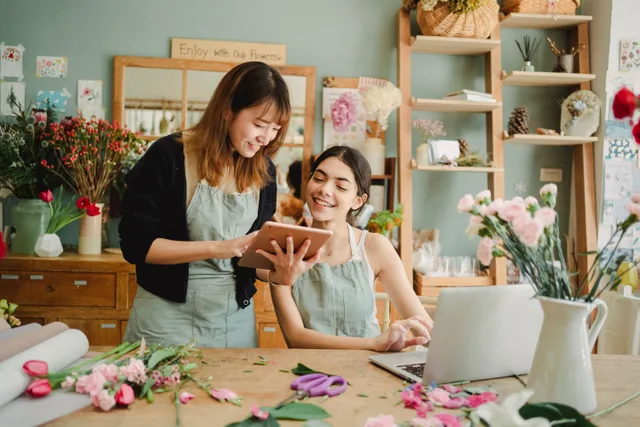 Content multiethnic female florists in aprons at table with laptop and browsing tablet while preparing for order in creative floristry studio. A local SEO checklist florists can actually run before ranking issues start